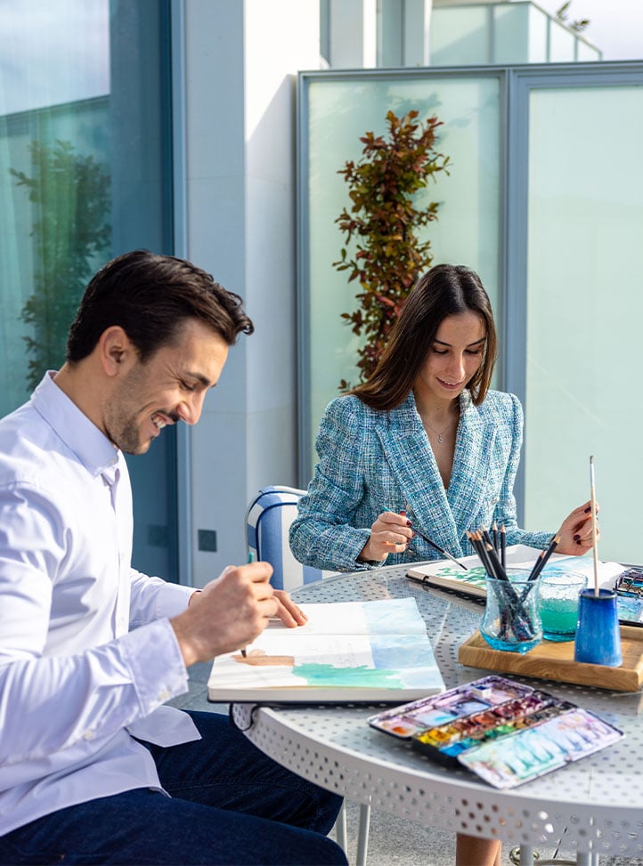 Couple painting with watercolours on a sunlit terrace.